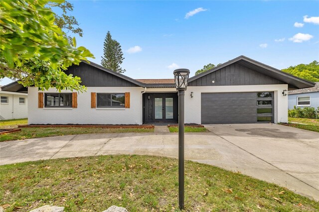 ranch-style home featuring concrete driveway, brick siding, a garage, and french doors