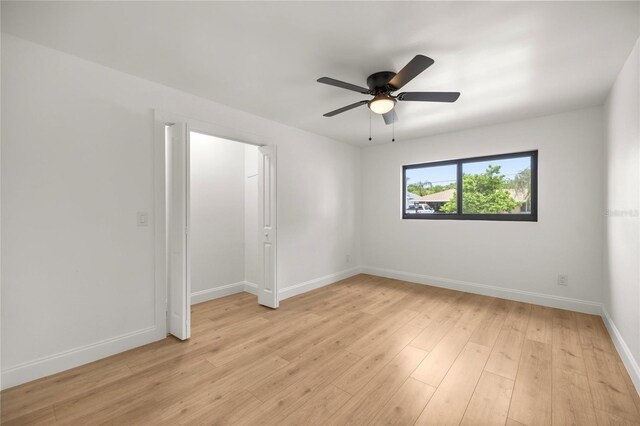 spare room with light wood finished floors, a ceiling fan, and baseboards