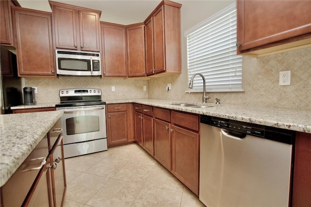 kitchen featuring a sink, tasteful backsplash, appliances with stainless steel finishes, light stone counters, and light tile patterned floors