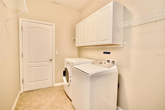 laundry area with washing machine and clothes dryer, baseboards, light tile patterned floors, and cabinet space