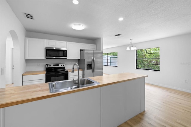 kitchen with wood counters, stainless steel appliances, visible vents, and a sink