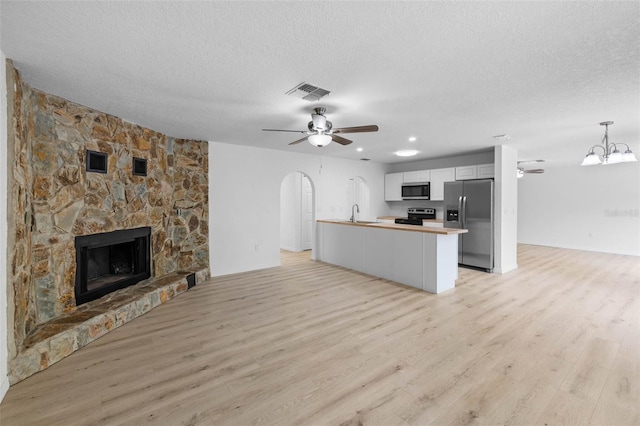 unfurnished living room with visible vents, arched walkways, a fireplace, a textured ceiling, and ceiling fan with notable chandelier