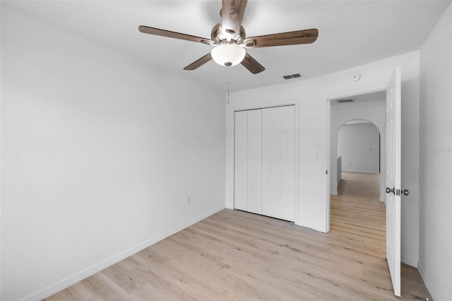 unfurnished bedroom with light wood-style flooring, arched walkways, baseboards, visible vents, and a closet