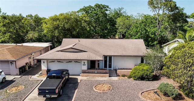 ranch-style home featuring a shingled roof, an attached garage, brick siding, stucco siding, and driveway