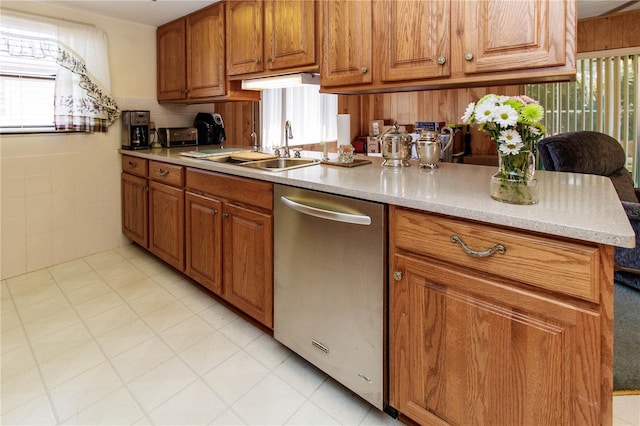 kitchen with stainless steel dishwasher, tile walls, brown cabinetry, and a sink