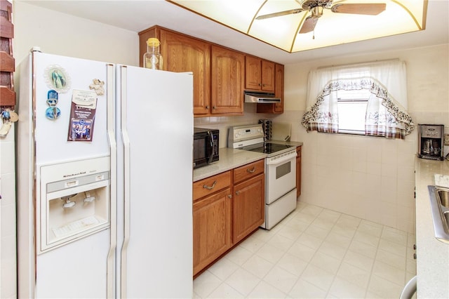kitchen featuring brown cabinetry, a ceiling fan, light countertops, under cabinet range hood, and white appliances