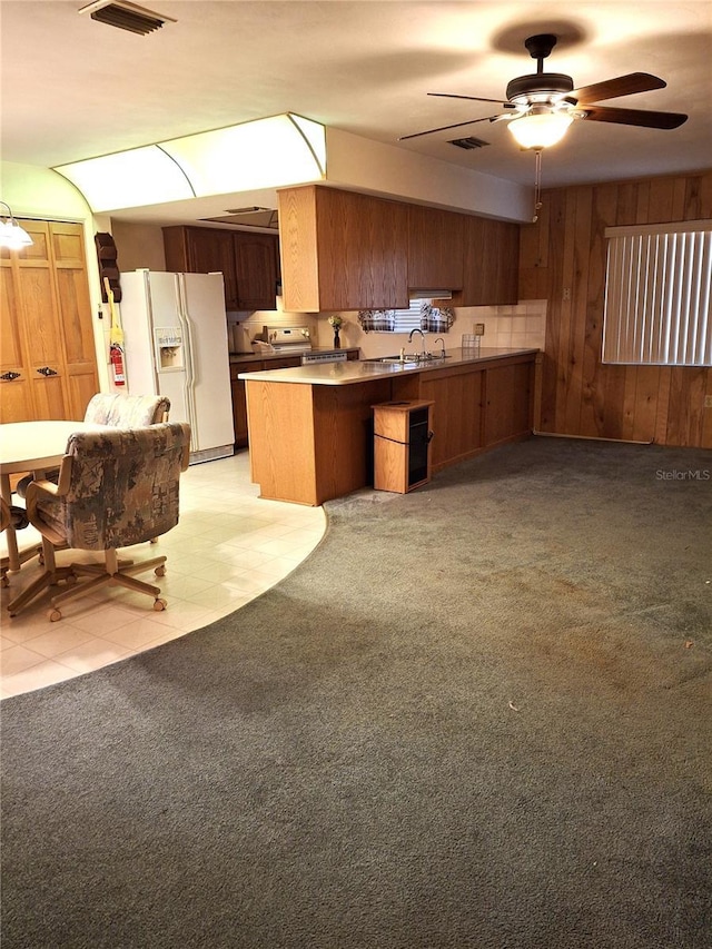 7715 Gulf Highlands Dr, Port Richey, FL 34668 - kitchen with white fridge with ice dispenser, a peninsula, a ceiling fan, wood walls, and brown cabinets
