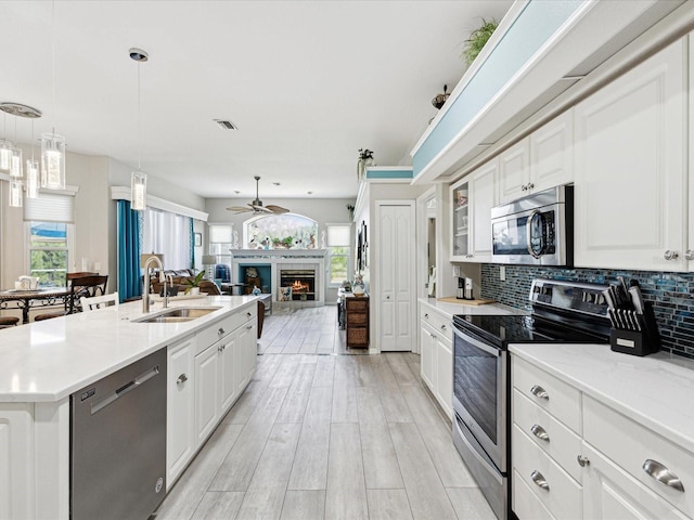 kitchen featuring white cabinets, a sink, stainless steel appliances, open floor plan, and a lit fireplace