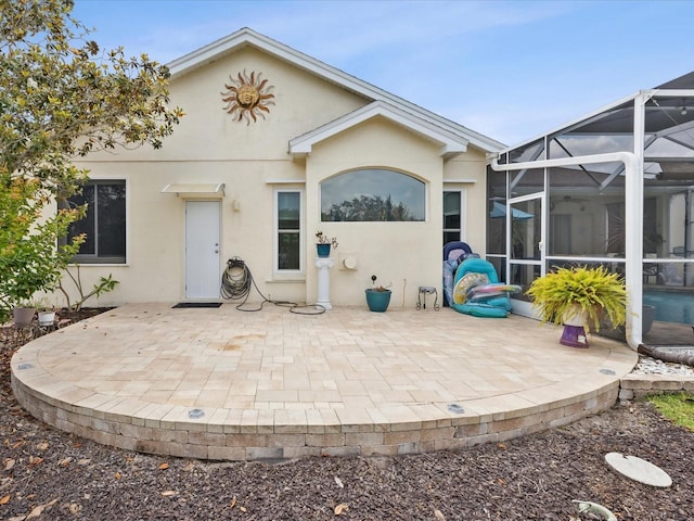 back of property with glass enclosure, a patio area, and stucco siding