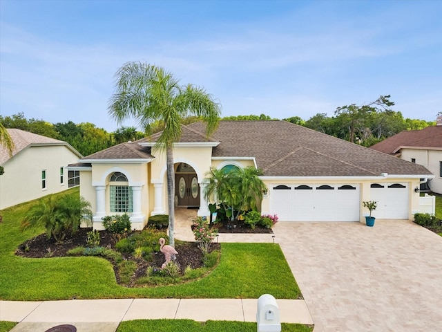 mediterranean / spanish-style house with a garage, decorative driveway, a front lawn, a shingled roof, and stucco siding