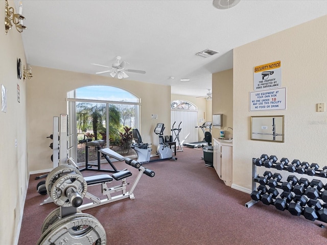 gym featuring baseboards, ceiling fan, visible vents, and dark colored carpet