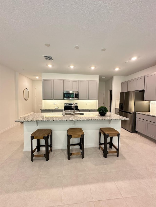 5236 Luisa Ct, Saint Cloud, FL 34771 - kitchen featuring stainless steel appliances, gray cabinets, a kitchen breakfast bar, light stone countertops, and recessed lighting