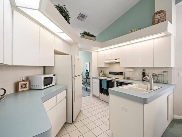 kitchen featuring a sink, under cabinet range hood, a peninsula, vaulted ceiling, and white appliances