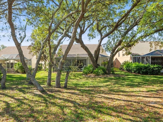 rear view of house featuring a sunroom, stucco siding, a tiled roof, and a lawn