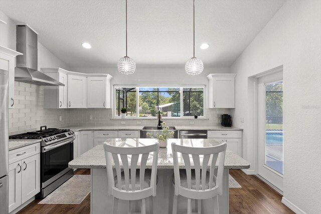 kitchen with white cabinets, a sink, wall chimney exhaust hood, stainless steel appliances, and decorative backsplash