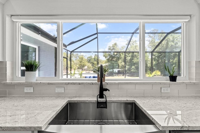 kitchen with a sink, light stone counters, decorative backsplash, and a sunroom