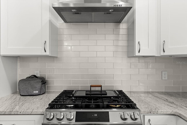 kitchen featuring white cabinets, backsplash, gas stove, and wall chimney range hood