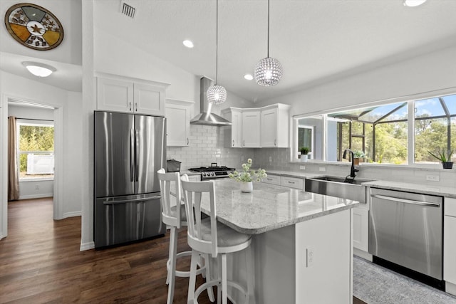kitchen with wall chimney range hood, visible vents, appliances with stainless steel finishes, a sink, and lofted ceiling