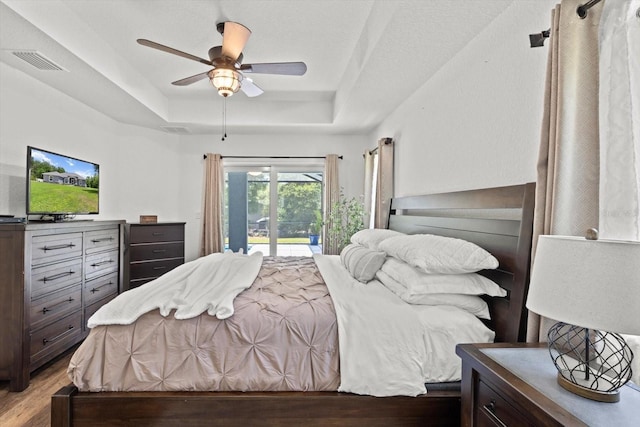 bedroom with visible vents, light wood-style floors, ceiling fan, access to outside, and a tray ceiling