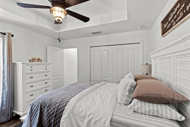 bedroom featuring ceiling fan, dark wood-style flooring, visible vents, a raised ceiling, and a closet