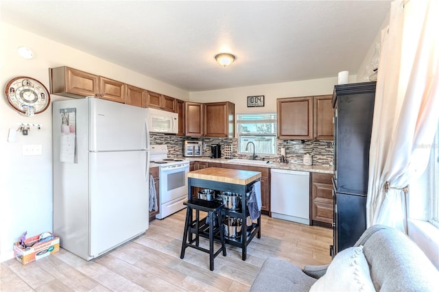 kitchen with backsplash, a sink, light countertops, light wood-style floors, and white appliances