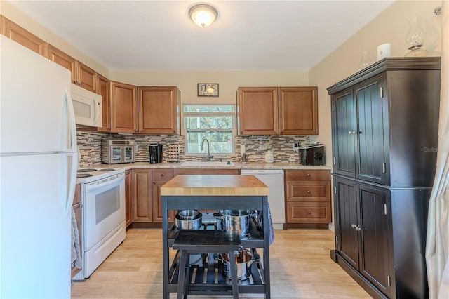 kitchen with a sink, decorative backsplash, light wood finished floors, and white appliances