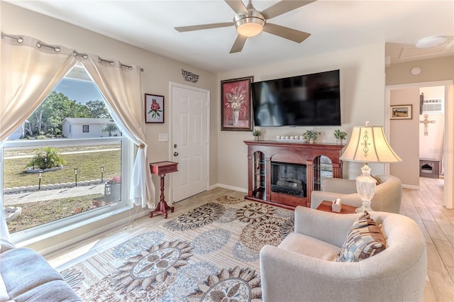 living area with a glass covered fireplace, baseboards, a ceiling fan, and light wood-type flooring