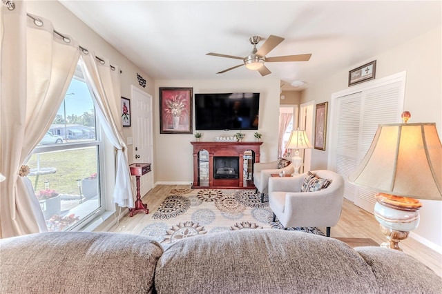 living area with baseboards, ceiling fan, a fireplace, and wood finished floors