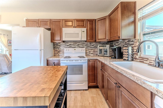 kitchen featuring decorative backsplash, white appliances, light wood-type flooring, brown cabinets, and a sink