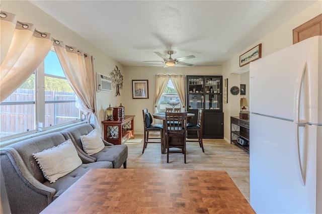 dining area with plenty of natural light, a ceiling fan, a wall unit AC, and light wood-type flooring