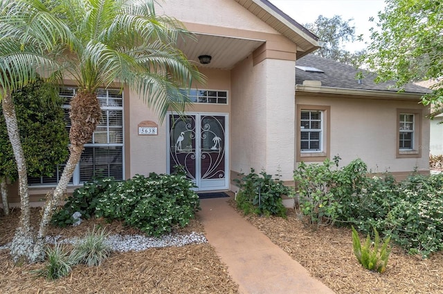 view of exterior entry featuring a shingled roof and stucco siding