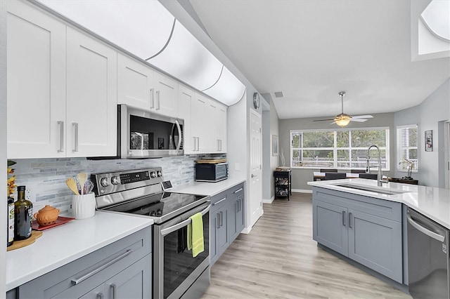 kitchen featuring appliances with stainless steel finishes, a sink, light countertops, decorative backsplash, and gray cabinetry