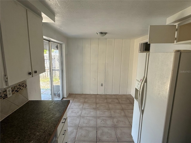 kitchen with decorative backsplash, light tile patterned flooring, white refrigerator with ice dispenser, dark countertops, and a textured ceiling
