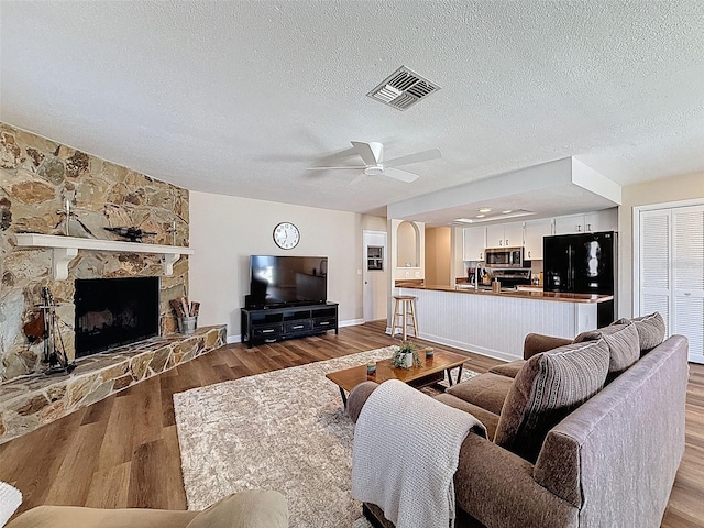 living room featuring ceiling fan, a fireplace, a textured ceiling, wood finished floors, and visible vents