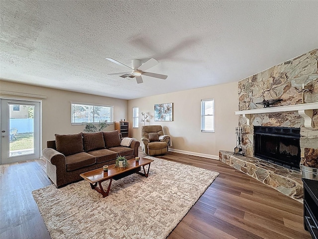 living area featuring wood finished floors, a fireplace, baseboards, ceiling fan, and a textured ceiling