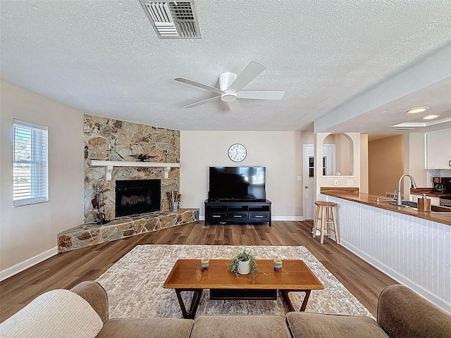 living room with a ceiling fan, visible vents, a fireplace, wood finished floors, and baseboards