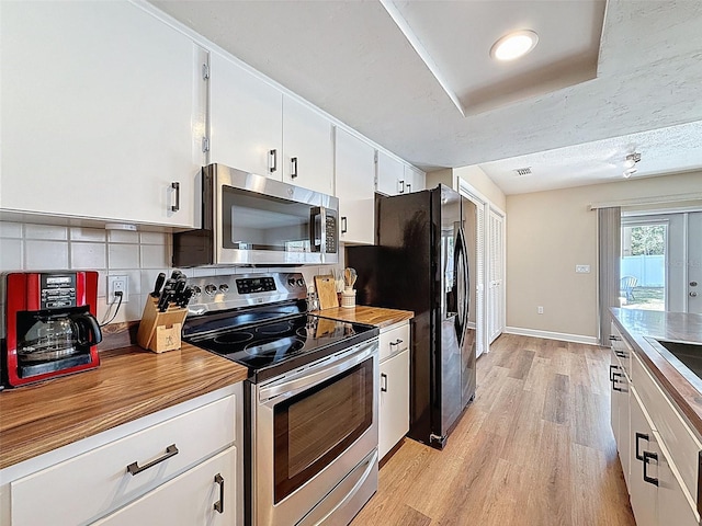 kitchen with visible vents, white cabinets, tasteful backsplash, light wood finished floors, and appliances with stainless steel finishes