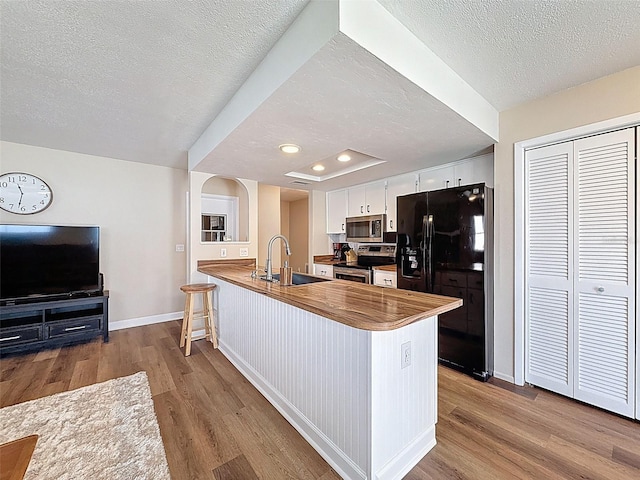kitchen featuring appliances with stainless steel finishes, a sink, a peninsula, baseboards, and wood finished floors