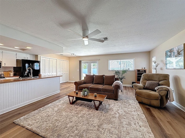 living room with a textured ceiling, ceiling fan, visible vents, and wood finished floors
