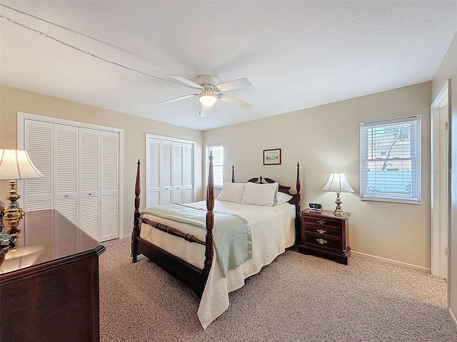 carpeted bedroom with two closets, ceiling fan, and baseboards