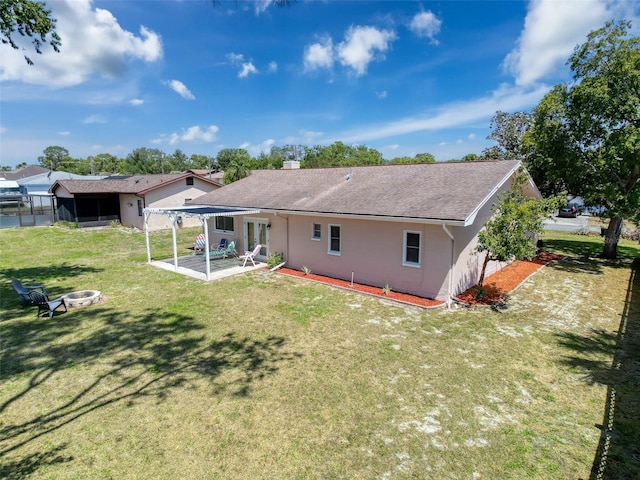 back of property featuring roof with shingles, stucco siding, a lawn, a patio, and a fire pit
