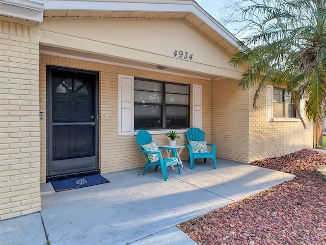 doorway to property featuring covered porch and brick siding