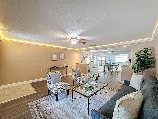 living area with baseboards, a textured ceiling, ceiling fan, and wood finished floors