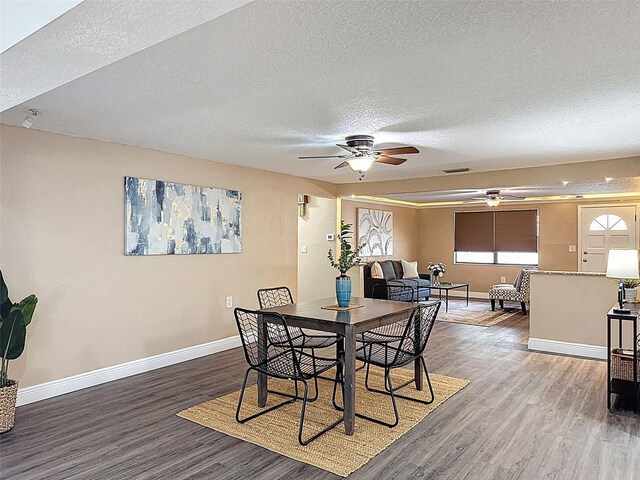 dining area featuring visible vents, wood finished floors, baseboards, a textured ceiling, and a ceiling fan