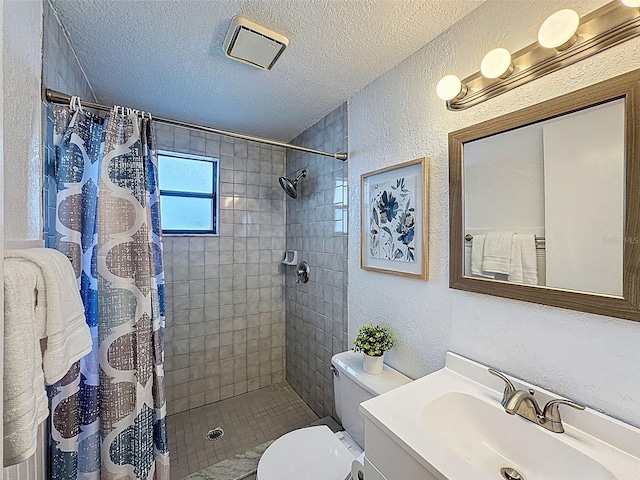 full bath featuring a textured wall, a tile shower, vanity, toilet, and a textured ceiling