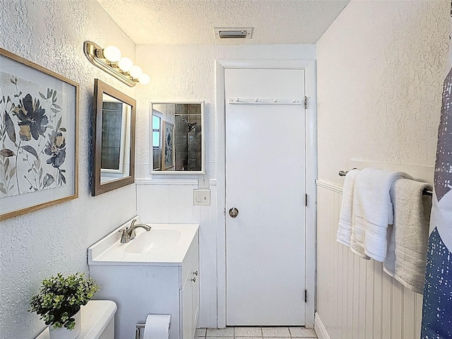 bathroom with a textured ceiling, visible vents, vanity, tile patterned floors, and a textured wall