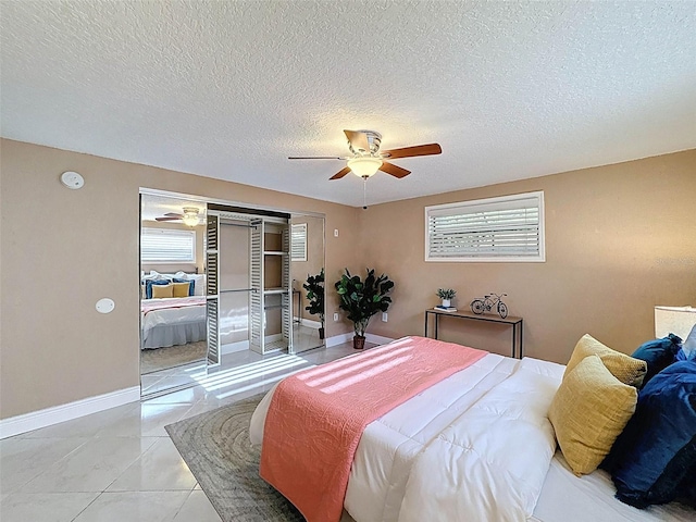 bedroom featuring a closet, baseboards, a textured ceiling, a ceiling fan, and light tile patterned floors