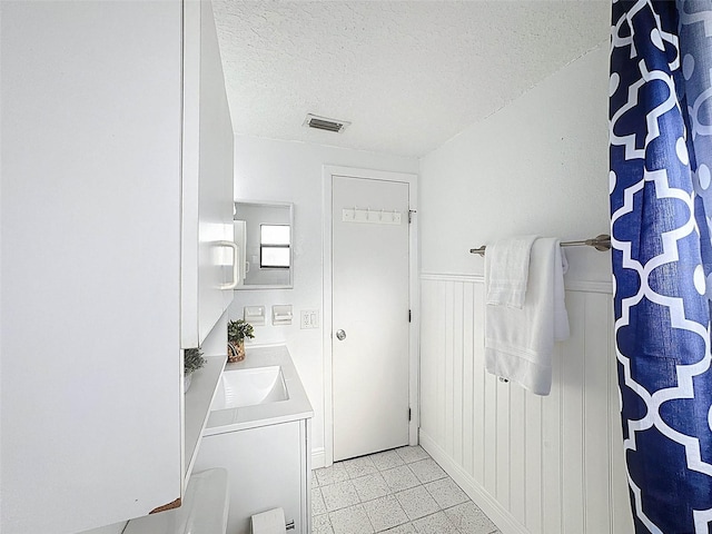 bathroom with visible vents, a textured ceiling, a wainscoted wall, and vanity