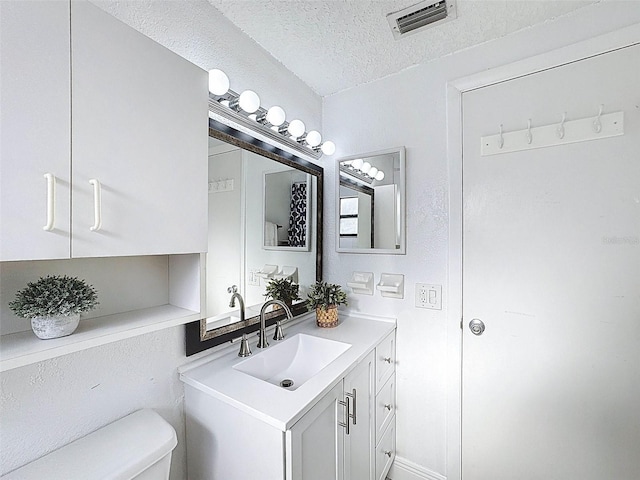 bathroom featuring toilet, a textured ceiling, visible vents, and vanity