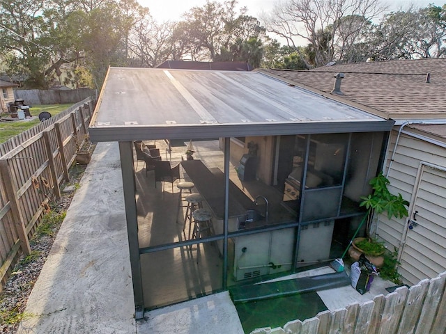 exterior space with roof with shingles, a fenced backyard, and a sunroom